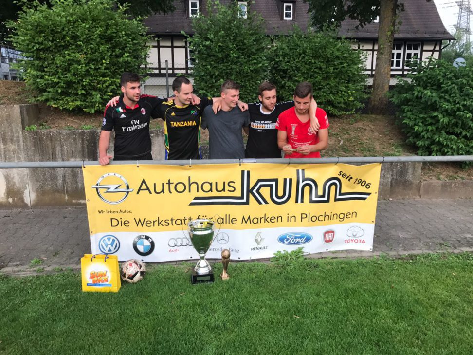 Fuenf Spieler mit Pokalen hinter dem Autohaus-Kuhn-Banner auf dem Sportplatz