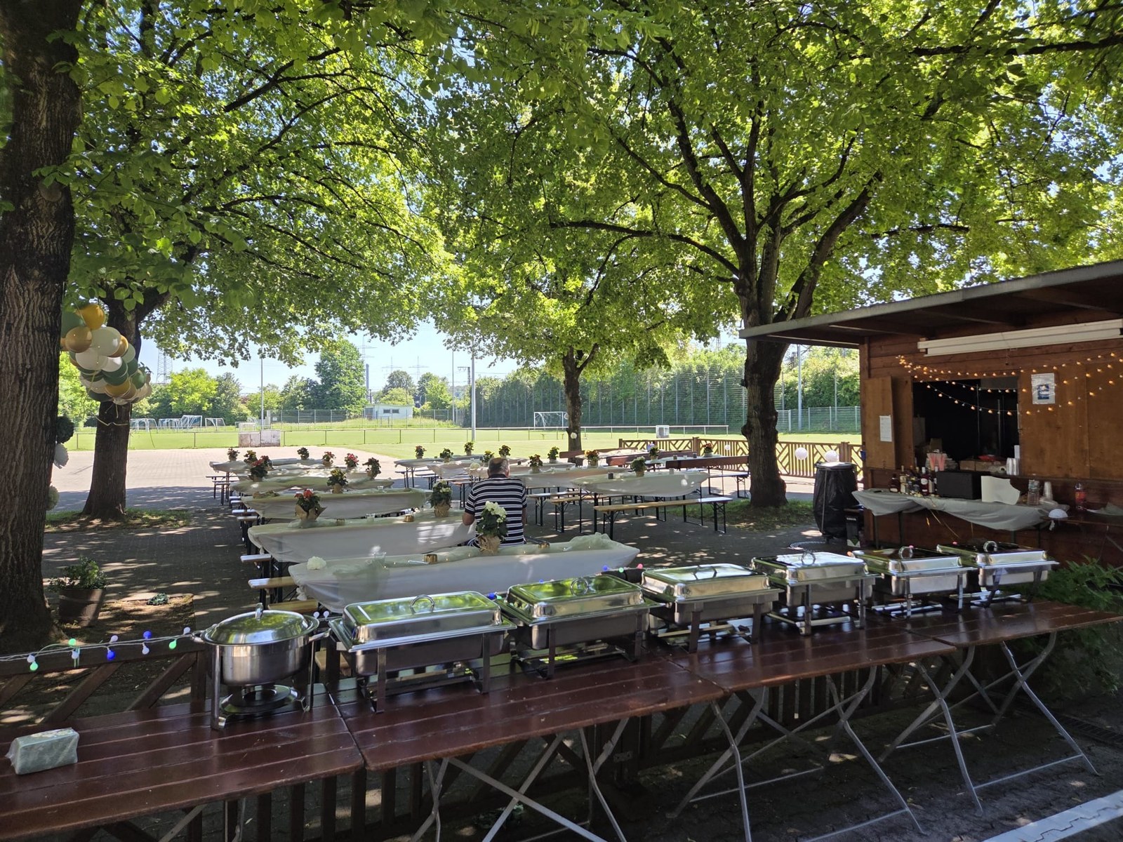 Außenbereich am Clubheim mit gedeckten Tischgarnituren und Buffet unter Bäumen